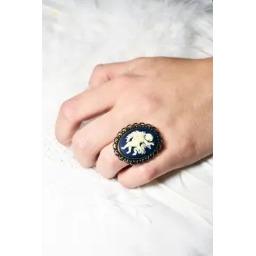 Bague au camée bleu nuit portée au doigt, main sur un linge blanc et des plumes