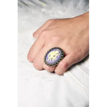 Bague au camée violet portée à la main, devant des plumes blanches
