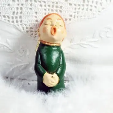 Figurine ange choriste roux en robe vert bouteille, de face, sur du linge brodé et des plumes