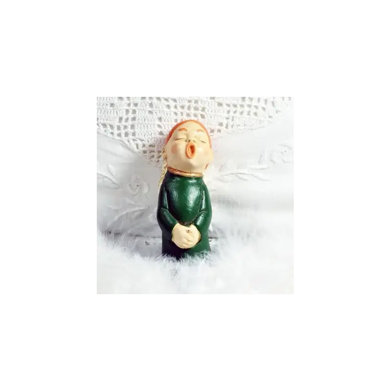 Figurine ange choriste roux en robe vert bouteille, de face, sur du linge brodé et des plumes