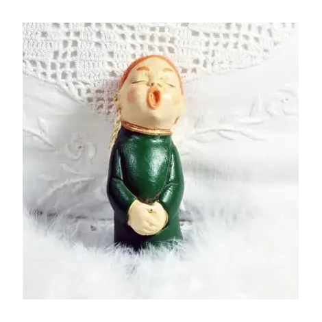 Figurine ange choriste roux en robe vert bouteille, de face, sur du linge brodé et des plumes