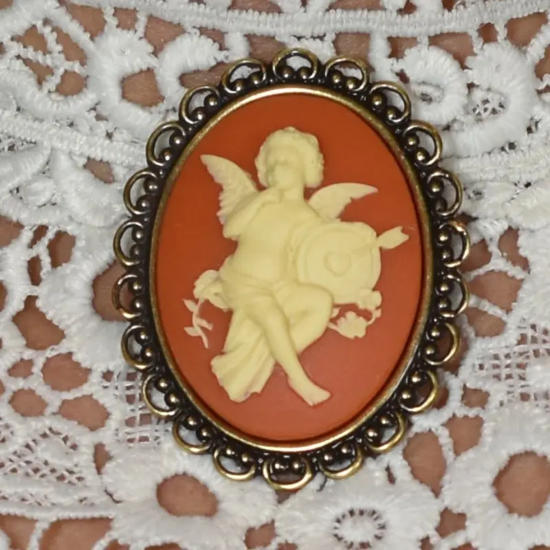 Broche camée fantaisie à l'ange « L'Amour », fond ambre, posée sur une dentelle