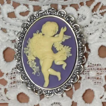 Broche camée vieil argent « La Danse » sur fond violet, posée sur une dentelle blanche