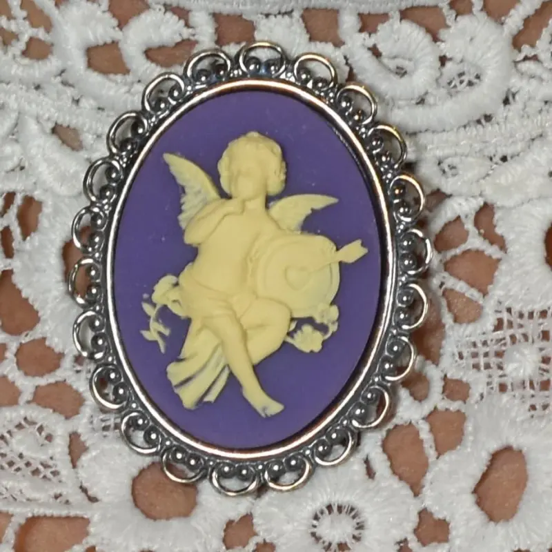 Le camée « L'Amour » sur fond violet, entouré de perles et de boucles de métal