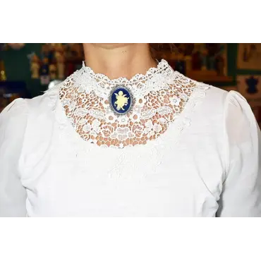 Portée au col, la broche bleu nuit se détache sur la dentelle blanche
