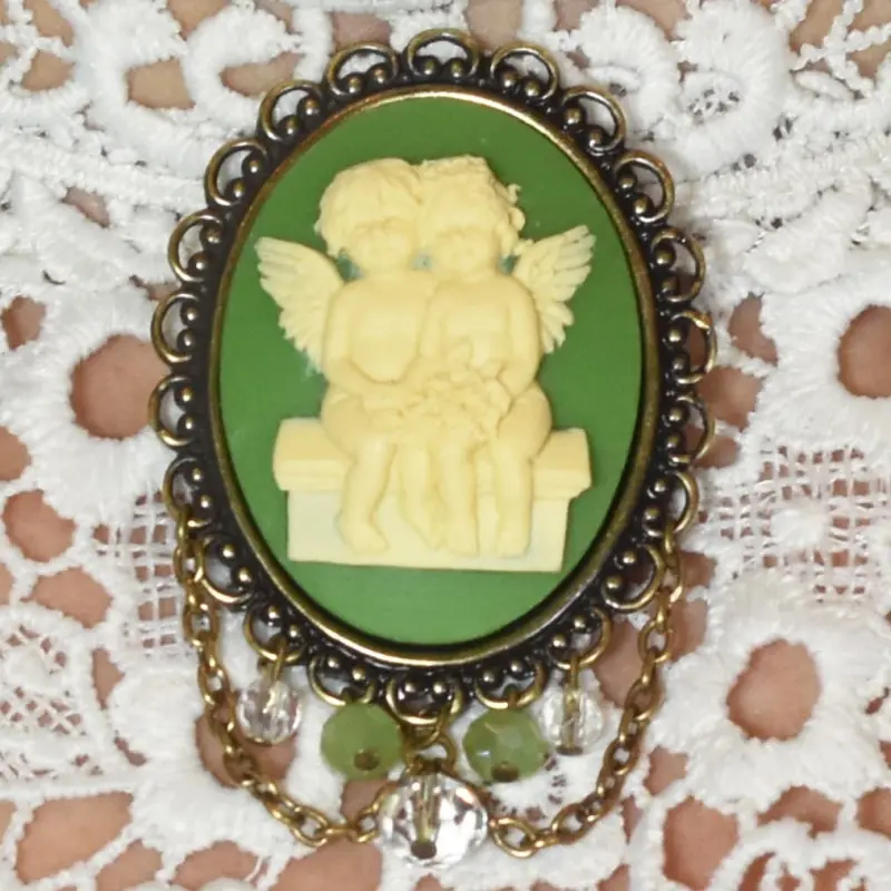 Broche châtelaine « Les Amoureux » vert olive, posée sur une dentelle blanche