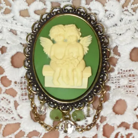 Broche châtelaine « Les Amoureux » vert olive, posée sur une dentelle blanche