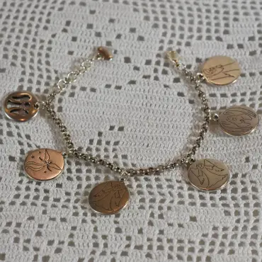 Gourmette ange argentée posée en rond sur dentelle au crochet, ses six médailles rondes autour