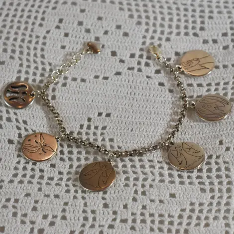 Gourmette ange argentée posée en rond sur dentelle au crochet, ses six médailles rondes autour