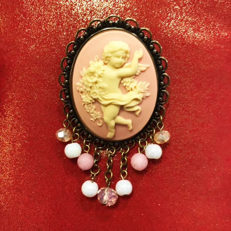 Broche châtelaine vieux bronze « La Danse » rose, posée sur un tissu rouge pailleté