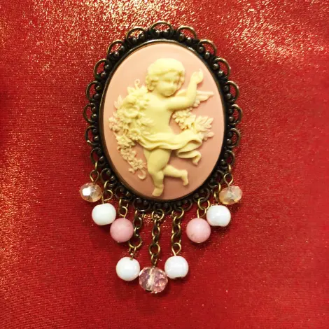 Broche châtelaine vieux bronze « La Danse » rose, posée sur un tissu rouge pailleté