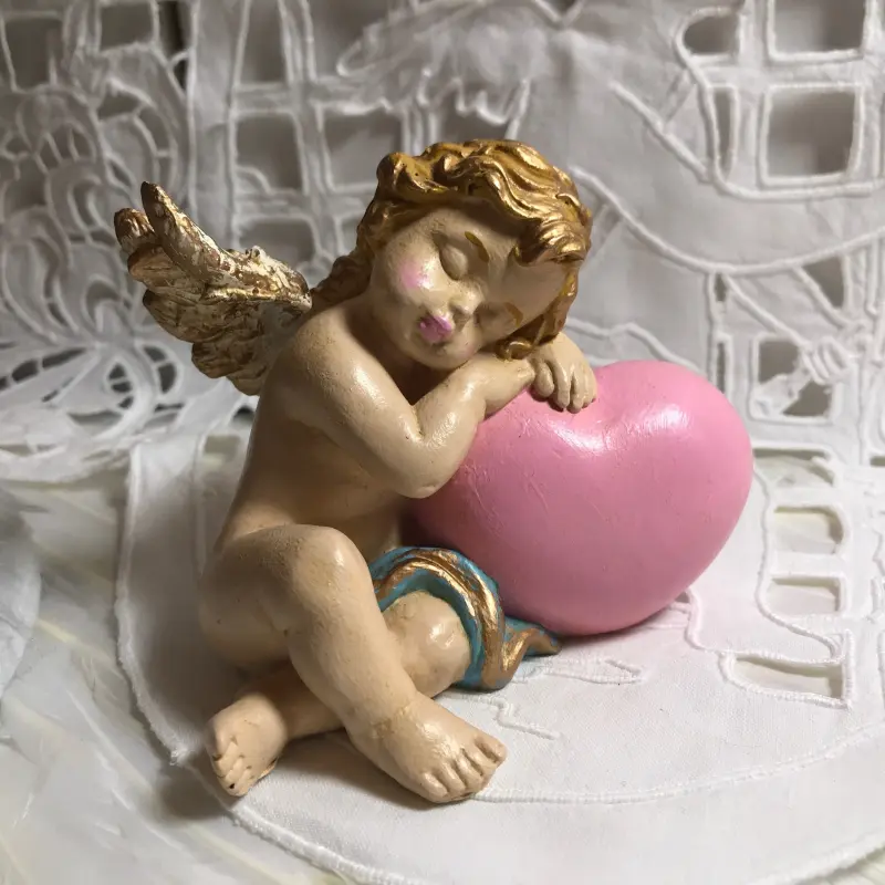 Figurine angelot endormi, la joue sur ses bras posés sur un gros cœur rose