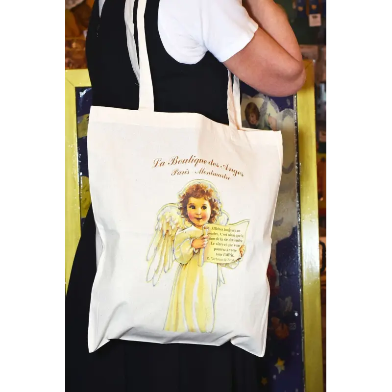 Tote bag citation « Le Sourire » porté à l'épaule, sur une robe noire et un tee-shirt blanc