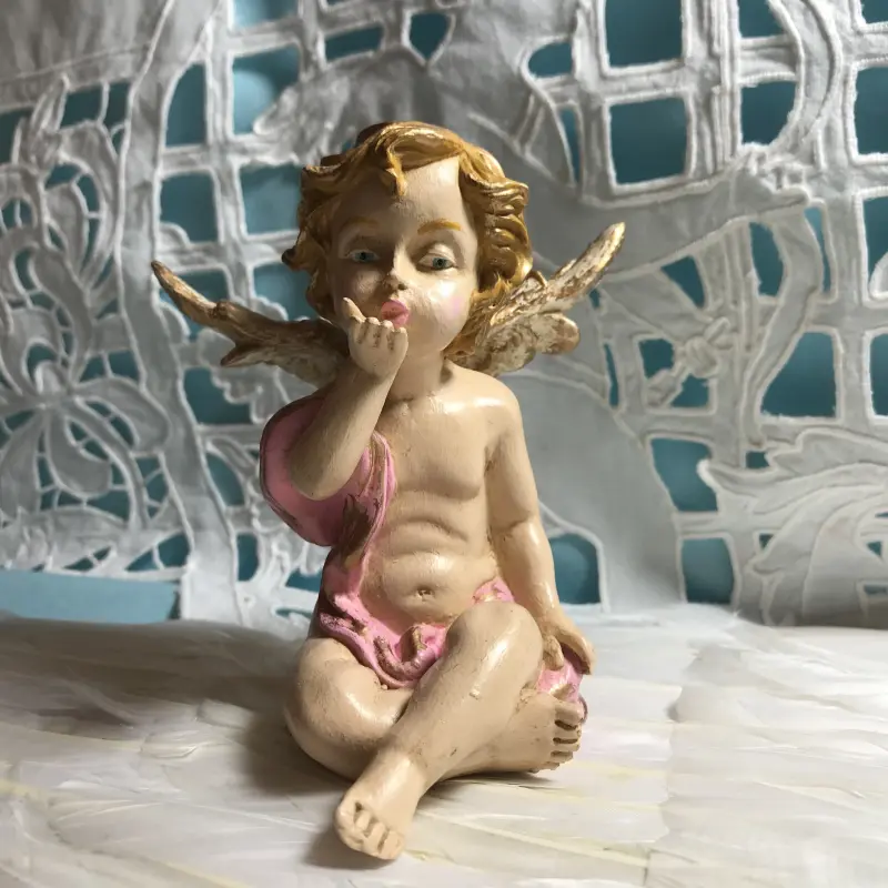 Statuette angelot au baiser, drapé rose, de face, assis, la main droite portée aux lèvres