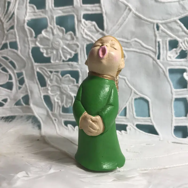 Figurine ange choriste vert printemps de face, mains jointes, devant une broderie ajourée